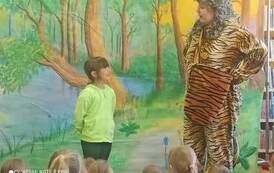 Na leśnym tle z przodu stoi przebrany w tygrysi str&oacute;j aktor i rozmawia z dziewczynką.