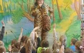 Na leśnym tle stoi przebrany aktor w tygrysim stroju i w zielonej czapce m&oacute;wiąc coś do dzieci.