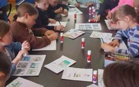 Dzieci siedzą przy stołach i przyklejają obrazki dotyczące etap&oacute;w powstawania książki