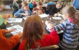 Dzieci siedzą przy stołach i układają historyjkę obrazkową, kt&oacute;rą poźniej przykleją.