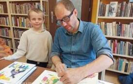 Autor książek dla dzieci &quot;Pan Poeta&quot; podpisuje chłopcu dedykację na książce.