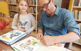 Autor książek dla dzieci &quot;Pan Poeta&quot; podpisuje dziewczynce dedykację na książce.
