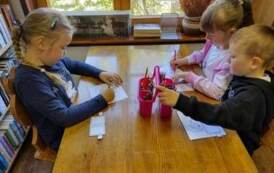 Dwie dziewczynki i chłopiec siedzą przy stole i kolorują obrazki.