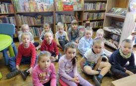 Grupa dzieci siedzących na siedziskach w Bibliotece.