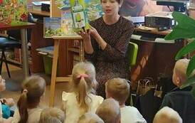 Dzieci siedzą na dywanie , a Pani Gosia z przodu pokazuje im zgniatarkę do plastkowych butelek.