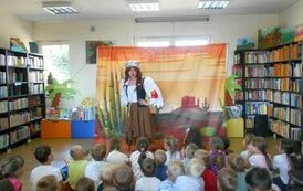 Aktorka przebrana za indiankę m&oacute;wi coś do widowni. W tle makieta przedstawiająca prerię.