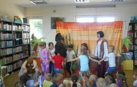 Część dzieci siedzi, a część tańczy w k&oacute;łeczku z aktorami przebranymi za indian. Widać pomiędzy nimi konika i żubra.