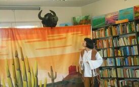 Aktorka przebrana za indiankę patrzy w g&oacute;rę na wychylającego się z nad makiety bawoła. Makieta przedstawia prerię.