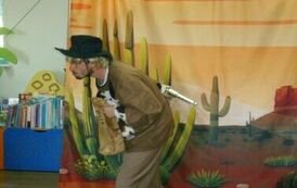 Aktor w kapeluszu pochylony z torbą w ręku. W tle widać pole i kaktusy.