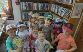 Dzieci stoja grupą przy drzwiach,  niekt&oacute;re z nich pokazują  swoje prace plastyczne.