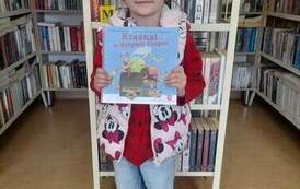 Dziewczynka w czapce z daszkiem stoi i trzyma książkę z wyprawki czytelniczej.