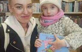 Dziewczynka stoi ze swoją mamą i trzyma w ręku książkę i kartę małego czytelnika.