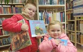 Chłopiec z dziewczynką trzymają w rękach swoje wyprawki czytelnicze, a chlopiec trzyma dodatkowo wypożyczoną książkę.Oboje się uśmiechają.