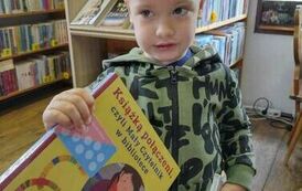 Chłopiec w blond włosach trzyma w rękach swoje nowe książki z wyprawki czytelniczej i kartę małego czytelnika na naklejki.