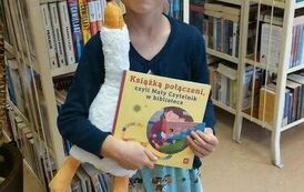 Dziewczynka w blond włosach pokazuje swoją nową książkę, trzyma jeszcze w ręku maskotkę gąskę.