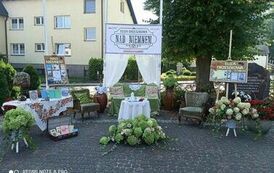 Pięknie przygotowany i przystrojony plac koło biblioteki z banerem, firankami, starymi meblami, książkami i kwiatami.