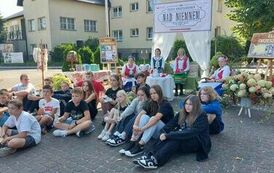 Na pięknie przystrojonym placu koło biblioteki siedzą Panie z KGW w strojach kociewskich,a przed nimi siedzi młodzież szkolna, kt&oacute;ra przyszła słuchać czytania.