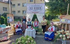 Na pięknie wystrojonym placu koło biblioteki siedzą Panie z KGW w strojach kociewskich, obok stoją dwie Panie bibliotekarki.
