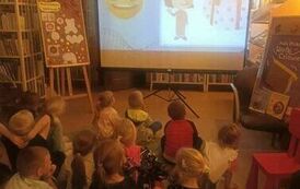 Dzieci siedzą na dywanie i oglądają bajkę na projektorze o Kropce.