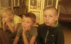 Trzech chłopc&oacute;w siedzi na dywanie i słucha bajki.