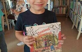 Chłopiec w czapeczce trzyma pokazując książkę o jesieni pt "Jesień plecień".