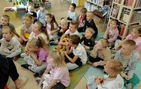Dzieci siedzą na dywanie, a Pani z biblioteki czyta im bajkę o jesieni.