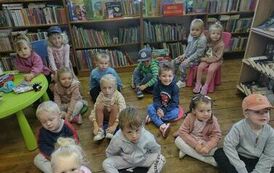 Dzieci siedzą na siedziskach i słuchają bajki czytanej przez Panią z biblioteki.