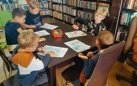 Chłopcy siedzą przy stoliku i kolorują na kartkach listki.