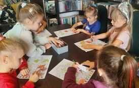 Dziewczynki siedzą przy stoliku i kolorują na kartce listki.