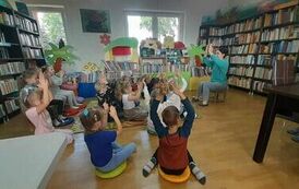 Dzieci siedzą dywanie i siedziskach i nasladują bibliotekarkę, kt&oacute;ra im pokazuje ćwiczenie na "skupienie się" z rączkami do g&oacute;ry.