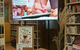 Na dużym ekranie telewizora wyświetla się film o powstawaniu książki, na dole jest stolik z książkami i małe dynie.