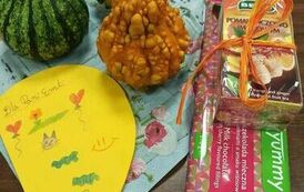 Na stole na serwetce leżą małe dynie, laurka od dzieci i czekolada z paczką herbaty.