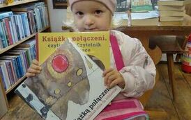 Dziewczynka trzyma w rękach swoje książeczki z wyprawki czytelniczej. Ma na sobie czapkę i torebkę.