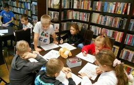 Dzieci siedzą przy dw&oacute;ch stołach i robią karty pracy.