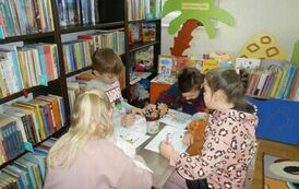 Czworo dzieci siedzi przy małym stoliczku i robią karty pracy.