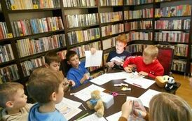 Dzieci siedzą przy stole i uzupełniają karty pracy.