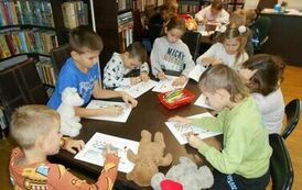 Dzieci siedzą przy dw&oacute;ch stołach i robią karty pracy.