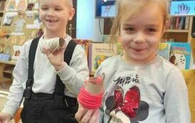 Chłopiec i dziewczynka stoją trzymając w rękach motki z nićmi. Za nimi duży ekran z wyświetlaną bajką o misiu.