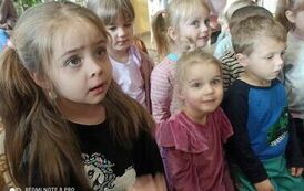 Dzieci siedzą na dywanie i słuchają bibliotekarki.