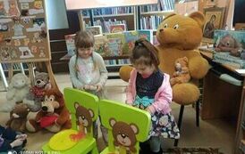 Dwie dziewczynki trzymają w rękach motki nici. Stoją przed małymi zielonymi krzesełkami na kt&oacute;rych oparciach sa naklejone twarze misia z dziurką w ustach przez kt&oacute;rą przełożona jest nic. Na siedzeniach są miski z rozwiniętymi nićmi.