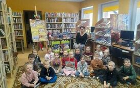 Zdjęcie grupowe dzieci siedzących na dywanie, z tyłu za nimi siedzi bibliotekarka.