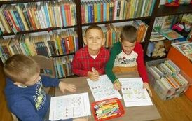Troje chłopc&oacute;w siedzi przy małym stolku i robią karty pracy.