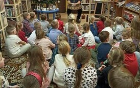 Dzieci siedzą na dywanie i patrzą na Szymona G&oacute;ralczyka, kt&oacute;ry im coś opowiada.