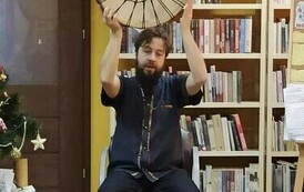 Szymon siedzi na krześle i trzyma uniesione do g&oacute;ry drewniane koło owinięte sznurkami.