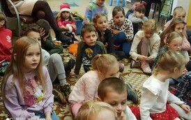 Grupa dzieci siedzących na dywanie i patrząca na występ Szymona.