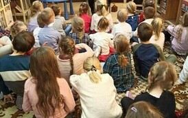 Dzieci siedzą na dywanie i patrzą na Szymona G&oacute;ralczyka, kt&oacute;ry im coś opowiada.
