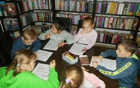 Dzieci siedzą przy stole i uzupełniają karty pracy.