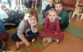 Dzieci siedzą na dywanie i słuchają bajki.