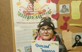 Dziewczynka w okularach pokazuje sw&oacute;j dyplom. Za nią jest tablica korkowa z plakatem promującym akcję MKWC i z innymi ciekawostkami kulturowymi.