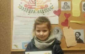 Dziewczynka pokazuje sw&oacute;j dyplom. Za nią jest tablica korkowa z plakatem promującym akcję MKWC i z innymi ciekawostkami kulturowymi.